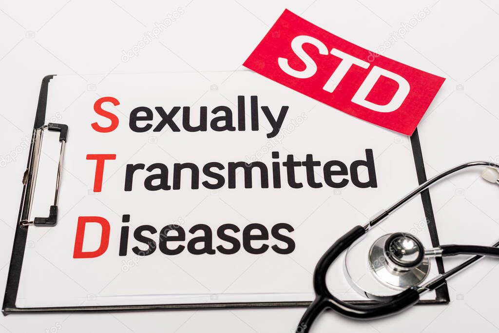 top view of clipboard with sexually transmitted diseases near red paper with std lettering and stethoscope isolated on white