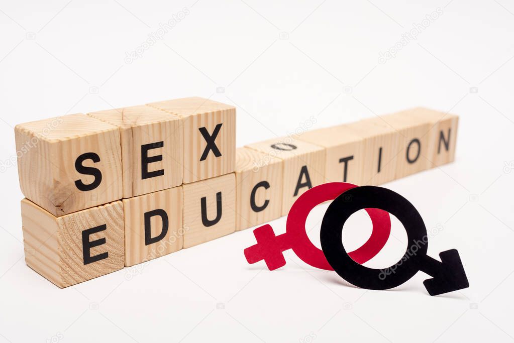 selective focus of wooden cubes with sex education lettering near gender symbols on white 