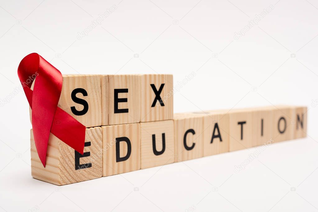 selective focus of wooden cubes with sex education lettering near red ribbon on white 