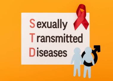 top view of paper people with male gender symbol near red ribbon and paper with sexually transmitted diseases lettering isolated on orange clipart