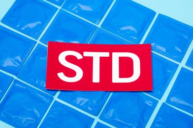 Mavi üzerine izole edilmiş prezervatif paketleri üzerinde STD harfleri olan kırmızı kağıdın üst görünümü