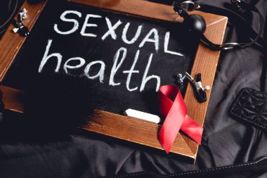chalkboard with sexual health lettering and sex toys and red ribbon on black silk  clipart
