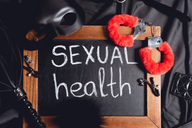 Siyah ipek üzerinde seks oyuncakları ve cinsel sağlık mektupları olan karatahtanın yanındaki maskenin üst görüntüsü 