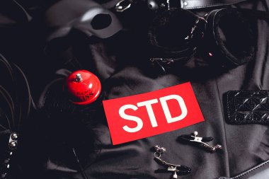 top view of red sex bell near paper with std lettering and sex toys on black  clipart