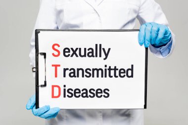 cropped view of doctor in latex gloves holding chalkboard with sexually transmitted diseases lettering isolated on grey  clipart