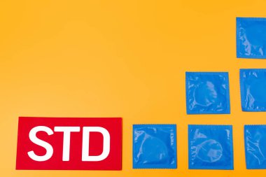 STD harflerinin yanındaki prezervatifli çantaların üst görüntüsü turuncu üzerine izole edilmiş. 