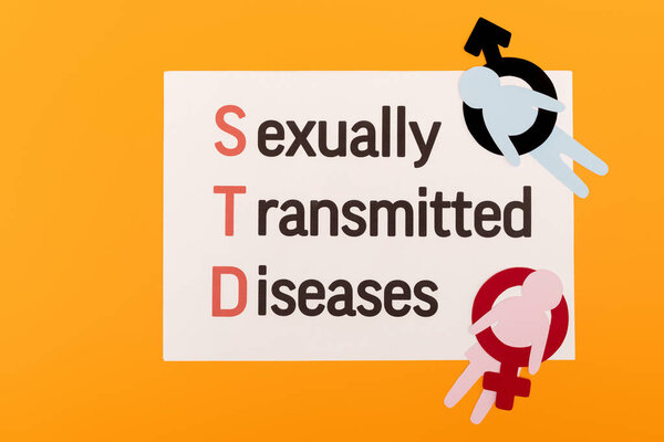 top view of paper people with gender symbols near paper with sexually transmitted diseases lettering isolated on orange