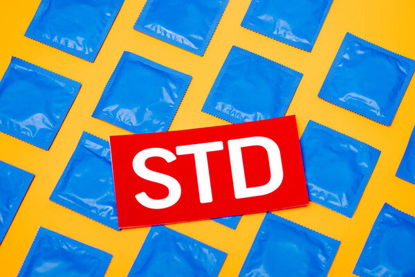 top view of paper with std lettering near blue packs with condoms isolated on orange 
