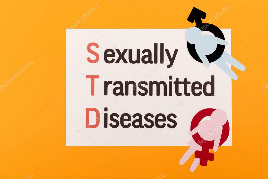 top view of paper people with gender symbols near paper with sexually transmitted diseases lettering isolated on orange