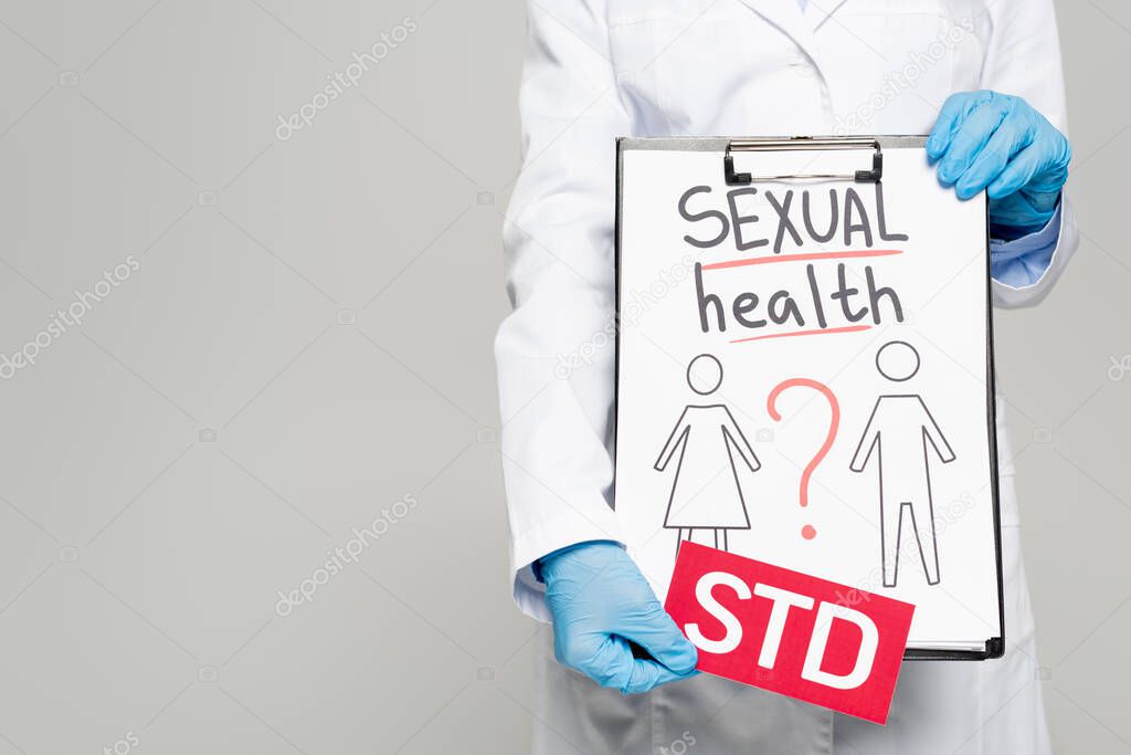 cropped view of doctor in blue latex gloves and white coat holding clipboard with sexual health, drawn man and woman and std lettering isolated on grey