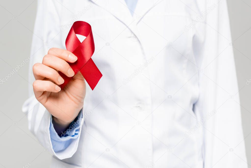 cropped view of doctor in white coat holding red ribbon isolated on grey 