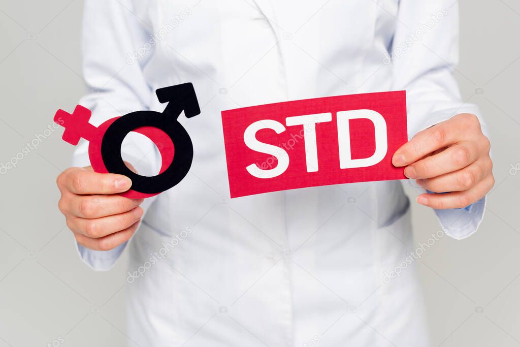 cropped view of doctor in white coat holding gender symbols and std lettering isolated on grey 