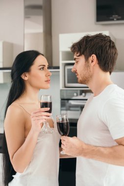 Kırmızı şarap bardaklı hassas çift evde yalnızlık çekerken birbirlerine bakıyorlar. 