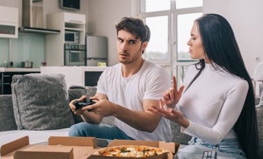 KYIV, UKRAINE - 16 Nisan 2020: Pizza ve joystickli güzel bir çift evde izolasyon sırasında kavga ediyorlar.