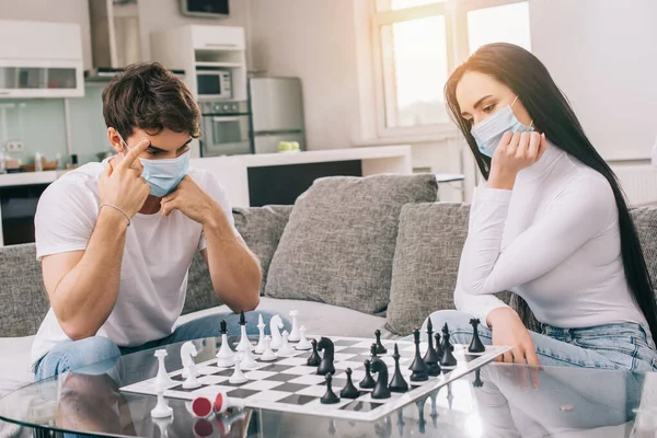 Больная пара в медицинских масках играет в шахматы дома во время самоизоляции — стоковое изображение Больная Пара Медицинских Масках Играет Шахматы Дома Время Самоизоляции — стоковое фото