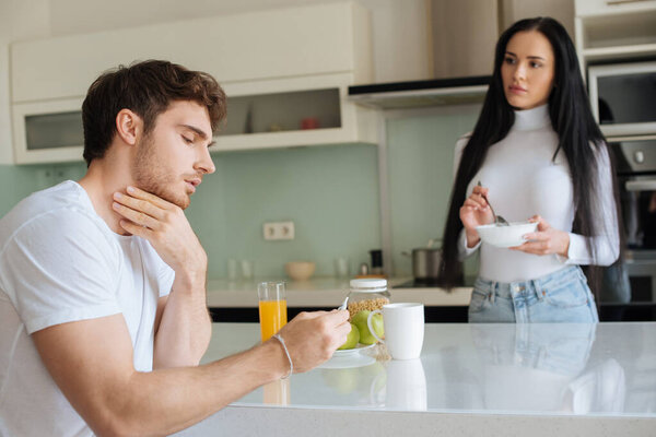 sick man looking at thermometer while worried woman holding bowl with breakfast at home during self isolation, selective focus