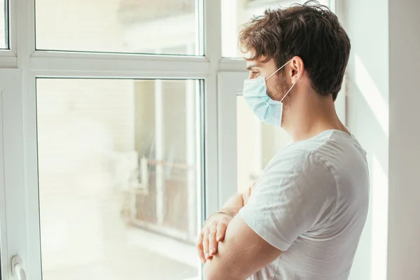 의료용 마스크를 슬픔에 남자가 자신을 고립시키는 창밖을 내다본다 — 스톡 사진