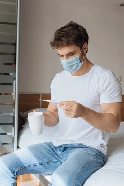 Λυπημένος Άρρωστος Άνθρωπος Ιατρική Μάσκα Κρατώντας Θερμόμετρο Και Κύπελλο Ζεστό — Φωτογραφία Αρχείου