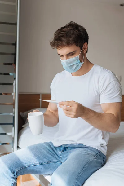 Triste Hombre Enfermo Máscara Médica Sosteniendo Termómetro Taza Con Bebida — Foto de Stock