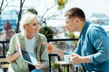 Sunny Terrace 'daki gülümseyen kadının yanındaki dizüstü bilgisayara bakan suratı olan adam.