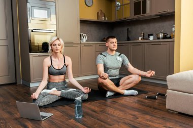 Genç çift, karantina sırasında evde dizüstü bilgisayarda birlikte yoga yapıyor.