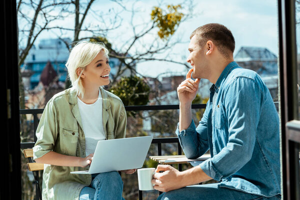 улыбающиеся фрилансеры, работающие с ноутбуком и пьющие чай на солнечной террасе
