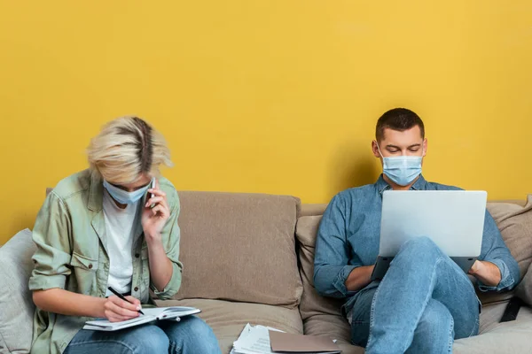 Young Freelance Couple Medical Masks Sofa Using Laptop Writing Notebook — Stock Photo, Image