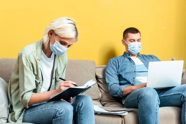 Joven Pareja Independiente Máscaras Médicas Sofá Utilizando Ordenador Portátil Escritura — Foto de Stock