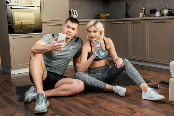 Young Couple Sitting Together Fitness Mat Sports Bottle Smartphone Home — Stock Photo, Image