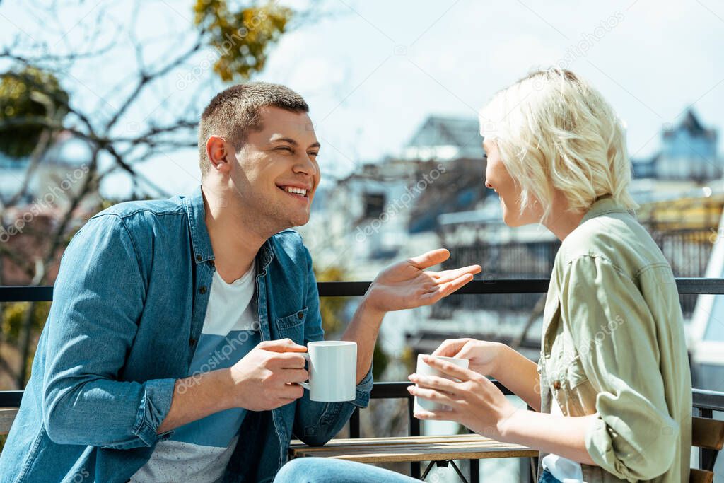 smiling couple talking and drinking tea on terrace