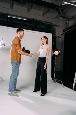 Side view of smiling model shaking hands with photographer in photo studio  clipart