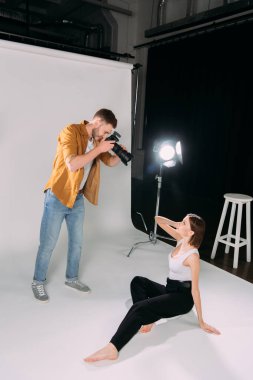Fotoğraf stüdyosunun zemininde güzel bir modelle çalışan fotoğrafçının yan görüntüsü. 