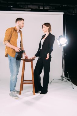 Fotoğraf stüdyosundaki şık modele bakan dijital kameralı fotoğrafçının yan görüntüsü 