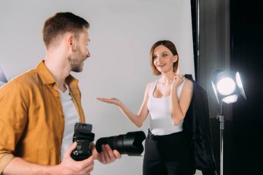 Gülümseyen manken ceketini tutuyor ve fotoğraf stüdyosundaki fotoğraf makineli fotoğrafçıyı işaret ediyor. 