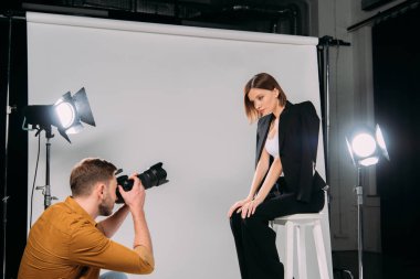 Fotoğraf stüdyosunda sandalyede oturan şık bir modelle çalışan fotoğrafçının yan görüntüsü. 