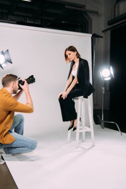 Fotoğraf stüdyosundaki fotoğrafçıya poz verirken sandalyede oturan güzel modelin yan görüntüsü. 