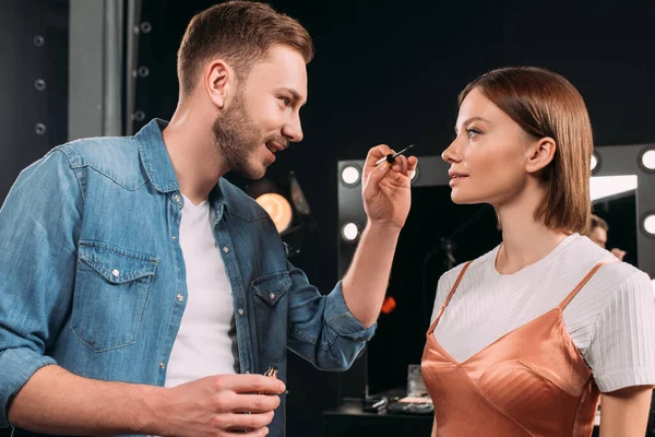 Sonriente Artista Maquillaje Sosteniendo Rímel Cerca Hermosa Modelo —  Fotos de Stock