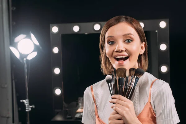 Modèle Joyeux Avec Des Pinceaux Cosmétiques Regardant Caméra Dans Studio — Photo