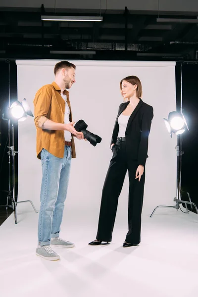 Fotógrafo Sorridente Segurando Câmera Digital Olhando Para Modelo Elegante Estúdio — Fotografia de Stock