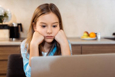 Sıkılmış çocuğun seçici odak noktası online çalışmak ve evde dizüstü bilgisayara bakmak.