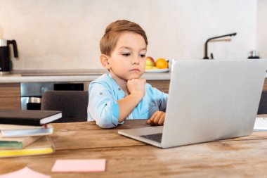 Evde e-öğrenim görürken dizüstü bilgisayara bakan sıkılmış çocuğun seçici odağı