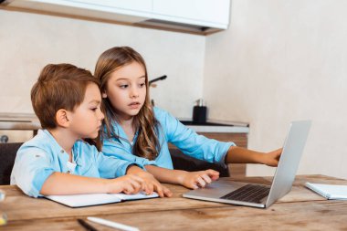 Evde e-öğrenim görürken dizüstü bilgisayara bakan kız ve erkek kardeşlerin seçici odağı