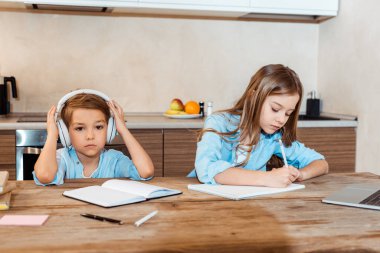 Evdeki kablosuz kulaklıkla kardeşinin yanına not defteri yazan bir çocuk.