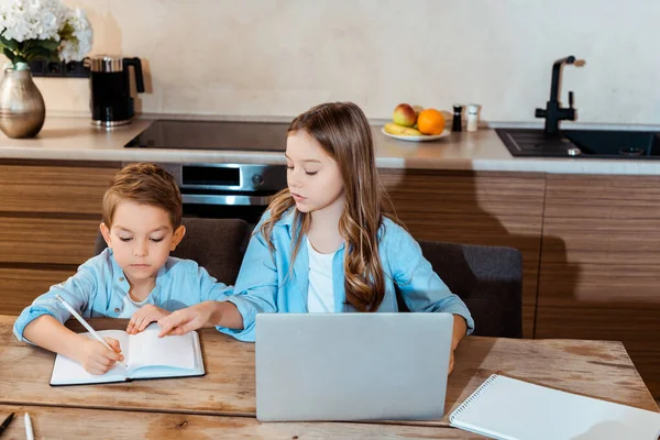 Siostra Patrząc Brata Piszącego Notatniku Przy Laptopie Podczas Learningu Domu — Zdjęcie stockowe