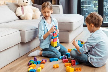 cute siblings playing with building blocks while sitting on floor in living room  clipart