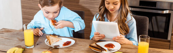 panoramic crop of boy eating toast bread with jam near sister using digital tablet 