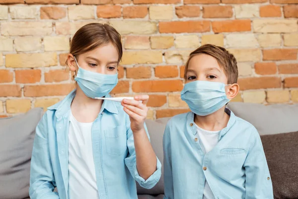 Beteg Gyerek Orvosi Maszkban Digitális Hőmérőt Tart Testvére Közelében — Stock Fotó