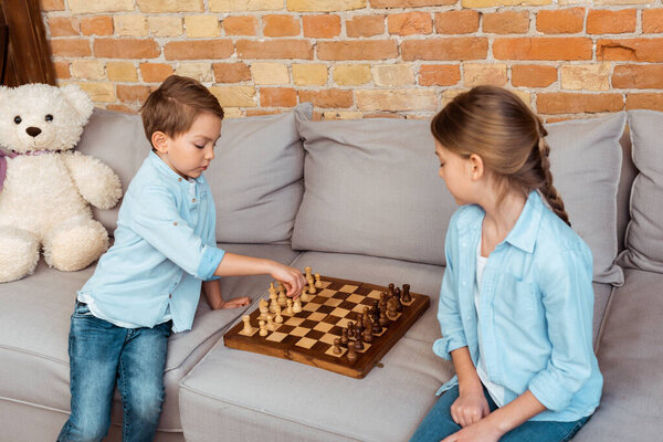 siblings playing chess on sofa in living room 