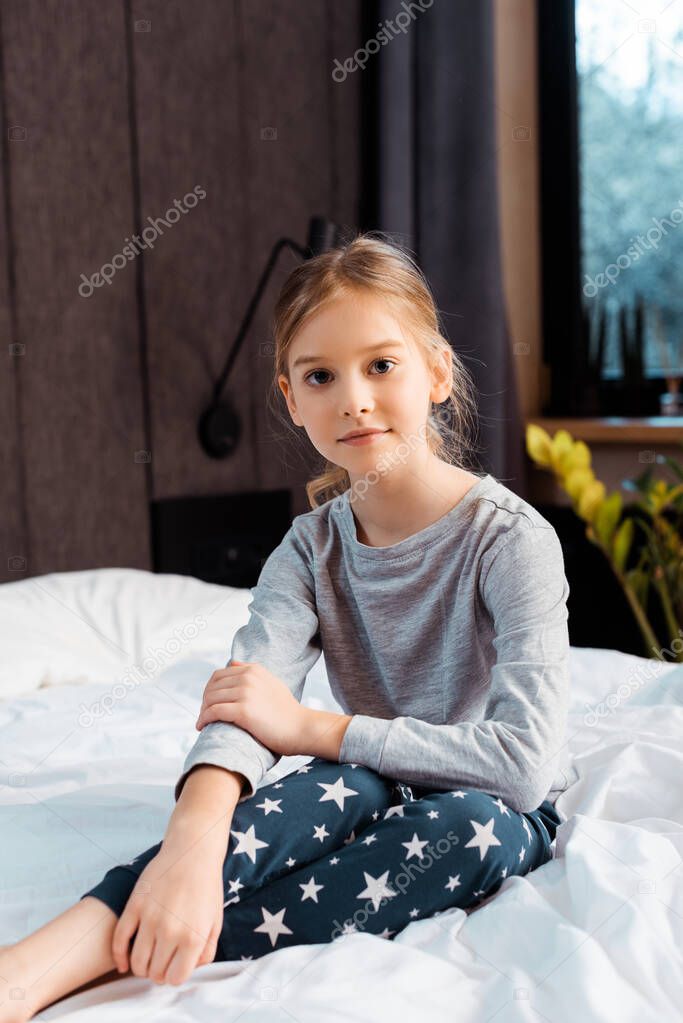 child looking at camera and smiling while sitting in bedroom 