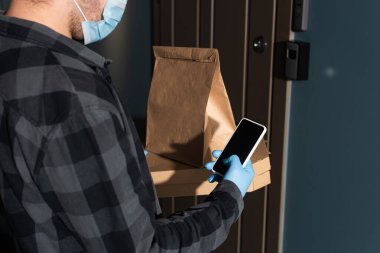Tıbbi maske takan kurye, pizza kutuları ve girişteki akıllı telefon görüntüsü.